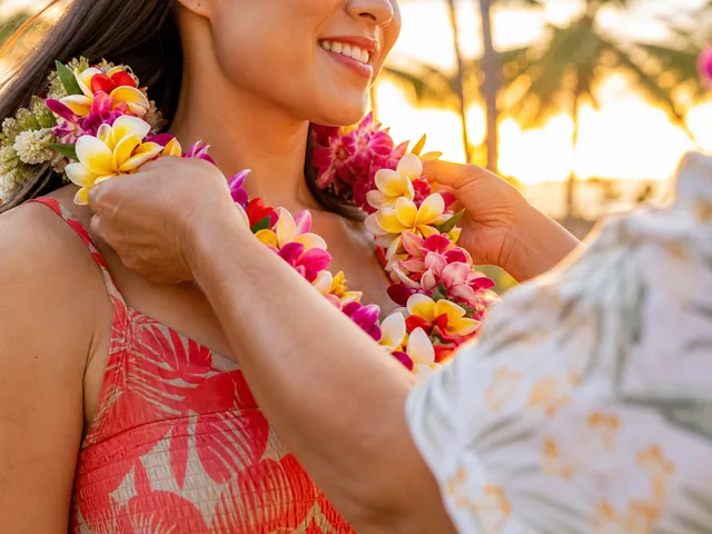Fresh plumeria and orchid lei being placed on a guest at sunset
